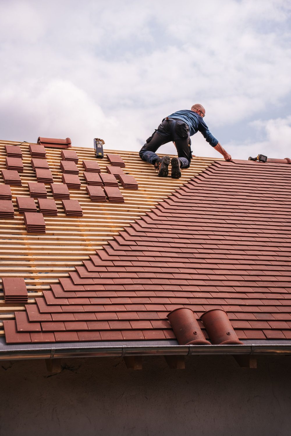 Roofer laying reddish clay roof tiles on battens